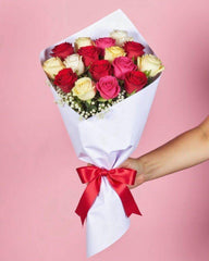 sixteen mixed roses and baby's breath with baby's breath. The flowers are wrapped in white tissue paper with a red ribbon.